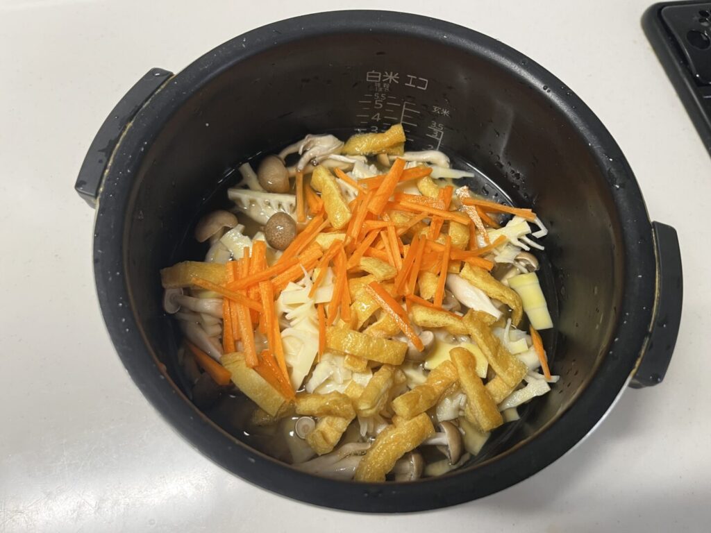 米の上に切ったたけのこと油揚げをのせた、炊く直前の状態