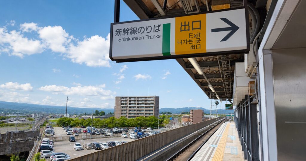 晴天の佐久平駅新幹線ホーム。ホーム上の「新幹線のりば」「出口」の案内看板と線路、その先に広がる佐久平の街並みや山並みが見渡せる。