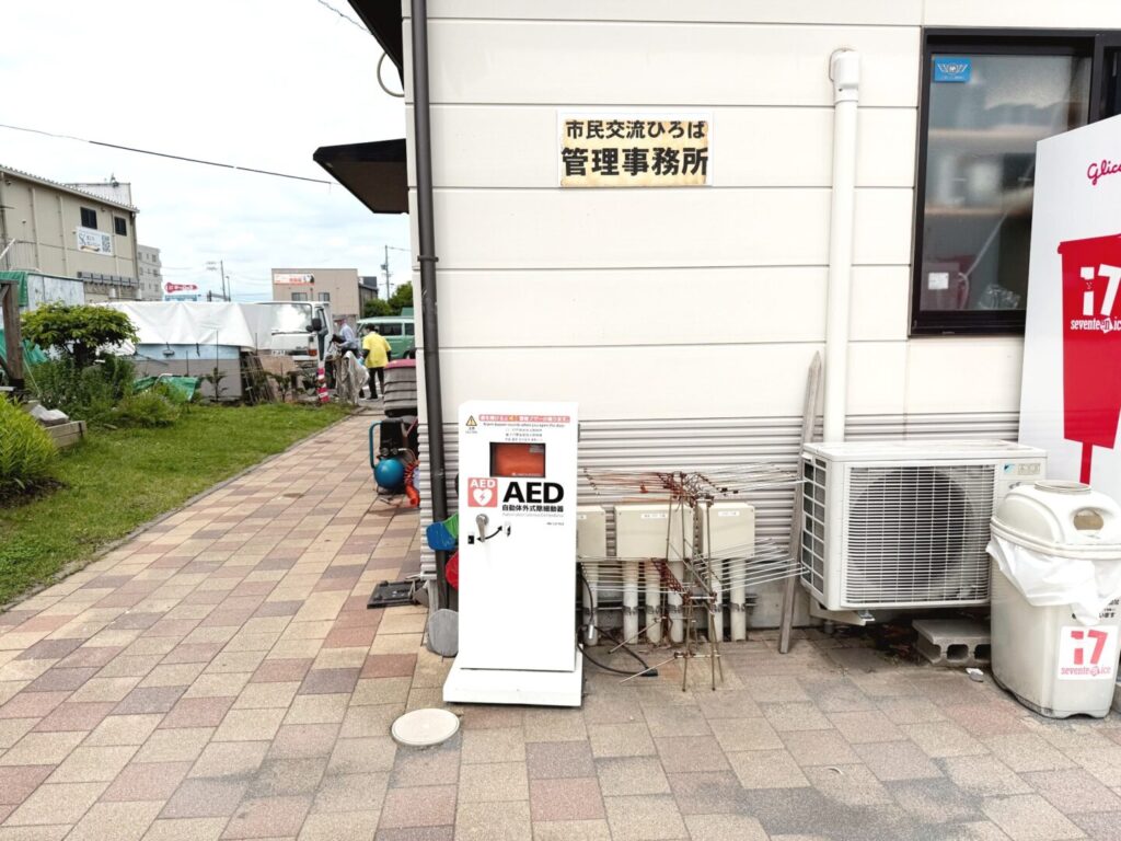 市民交流ひろば管理事務所の外壁前に屋外設置された白いAEDスタンドボックス