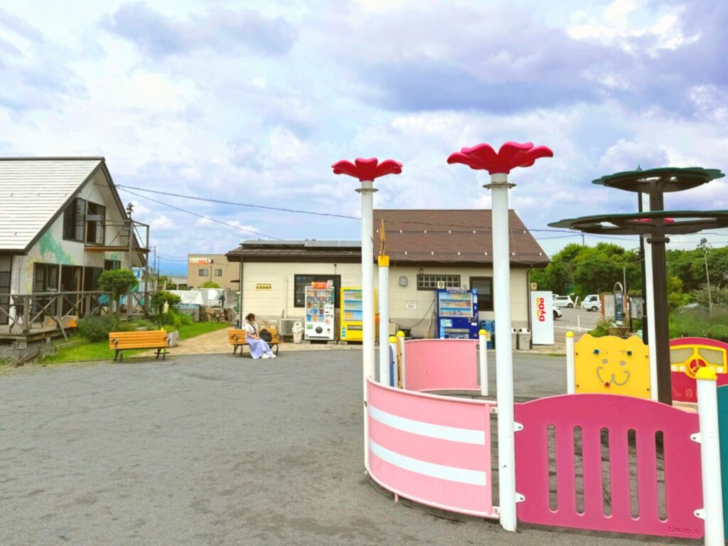 市民交流ひろばの園内から見た管理事務所方面。花の形のオブジェとピンクの幼児用遊具がある
