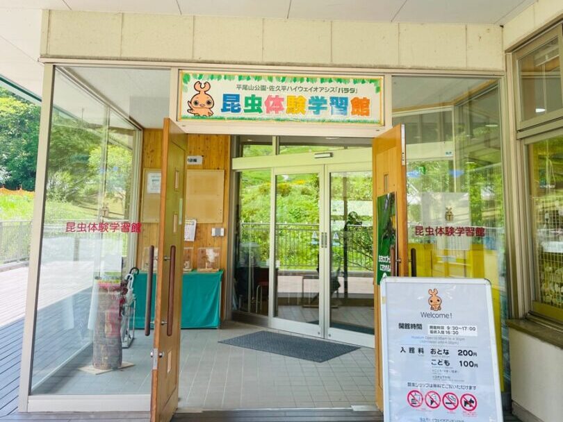 パラダ・昆虫体験学習館の入口。緑の看板とかわいい昆虫のキャラクター、入館料の案内板が出迎えてくれる