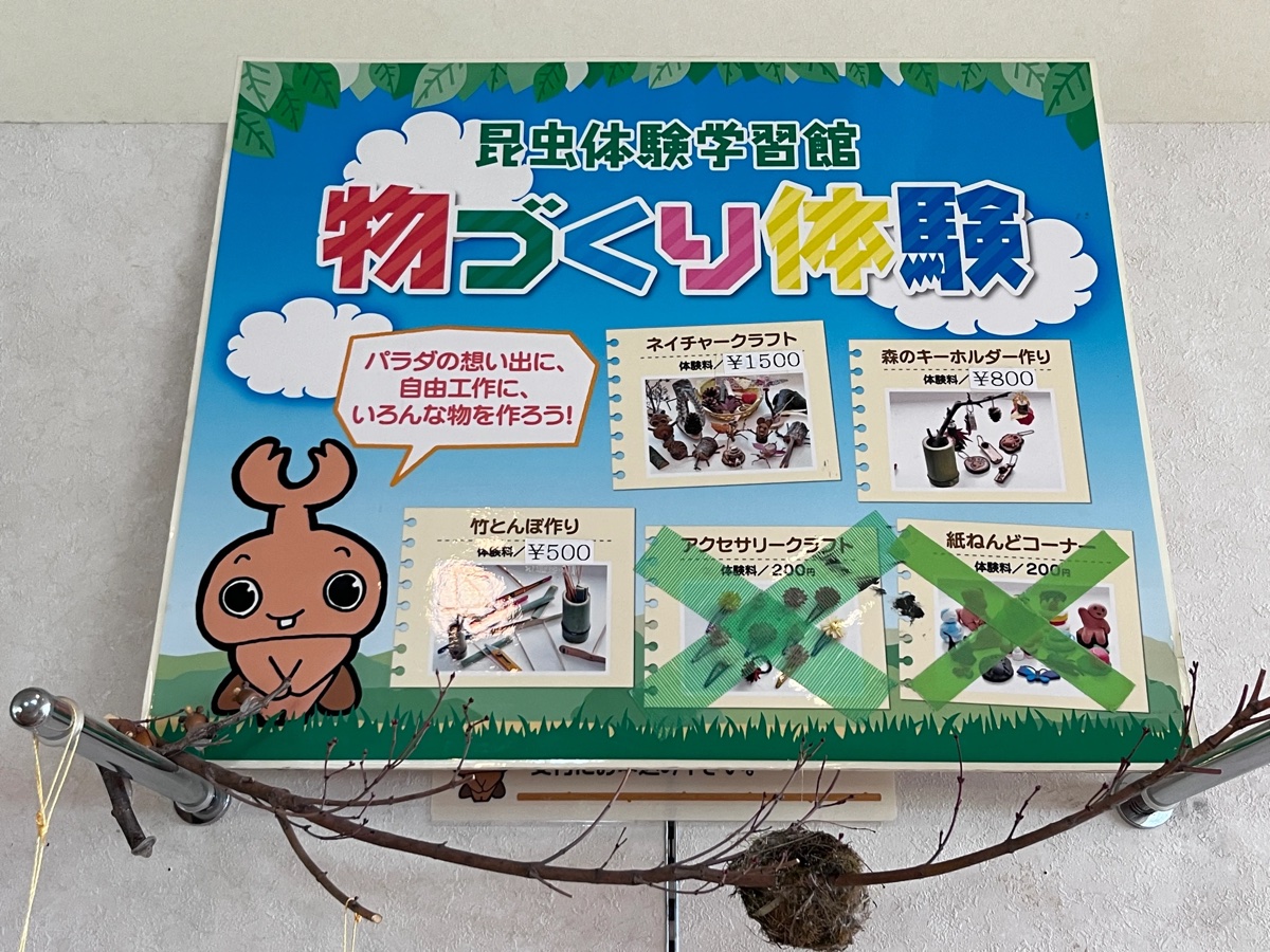 昆虫体験学習館「物づくり体験」のメニュー看板。ネイチャークラフトや森のキーホルダー作りなどの体験メニューと料金が書かれている