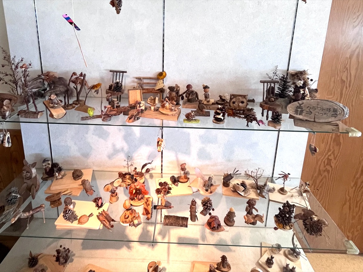 ガラス棚に並ぶ見本作品。松ぼっくりや木の実で作られたフクロウや動物たちのクラフトがぎっしり並ぶ