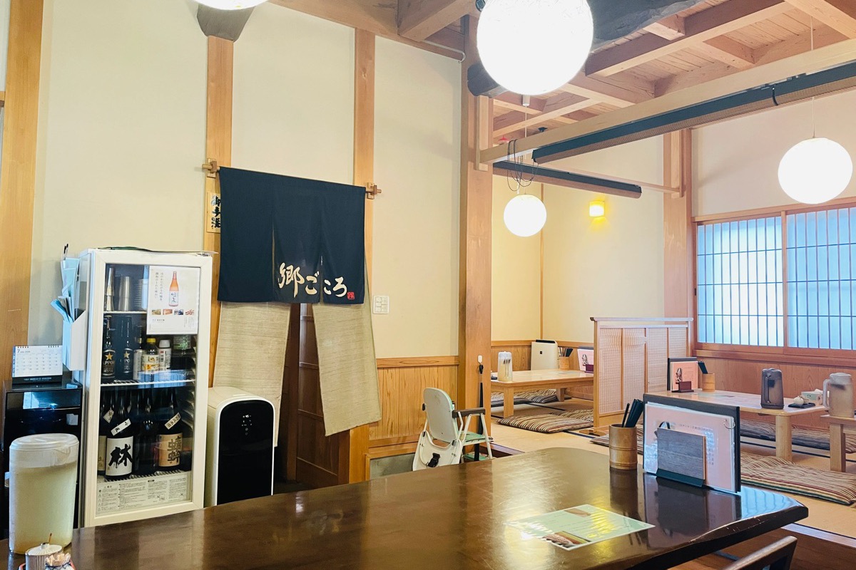 郷ごころの店内。木のぬくもりを感じるテーブル席の奥に、のれんと座敷席が見える落ち着いた和の空間