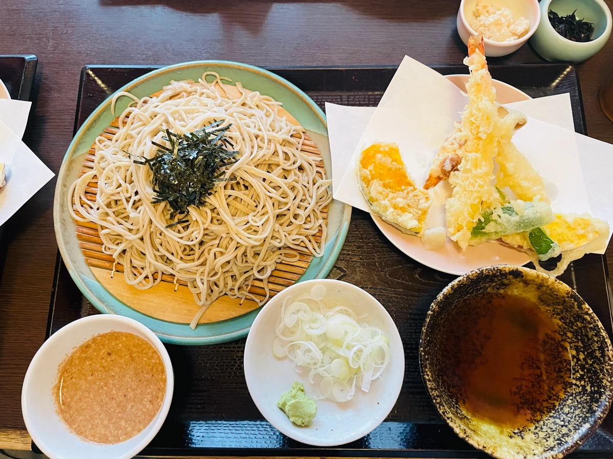 郷ごころの天ざるそば。ざるに盛られた手打ちそばに、海老と野菜の天ぷら、薬味のねぎとわさび、追加の胡桃だれが並ぶ