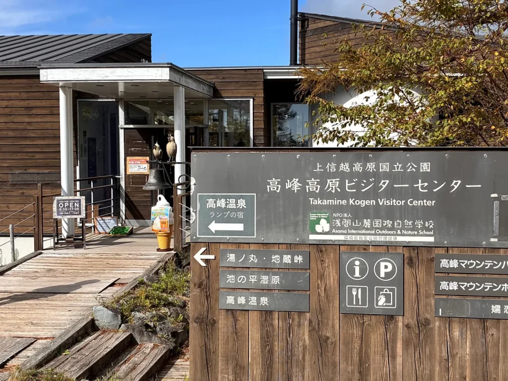 木造の高峰高原ビジターセンターの入口と、高峰温泉・池の平湿原などの案内看板