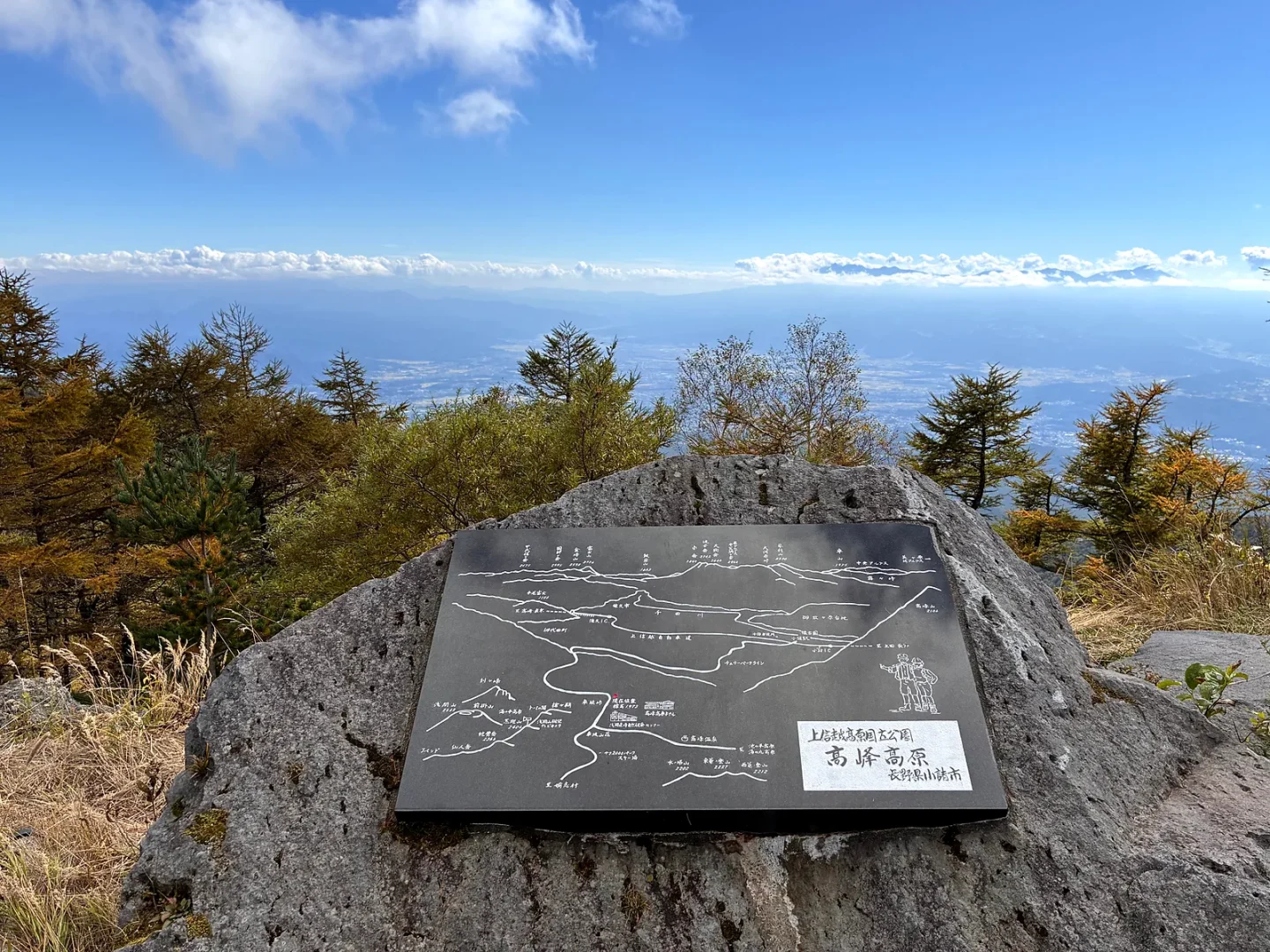 岩に据えられた高峰高原の展望盤。奥に雲海と、ふもとまで続く景色